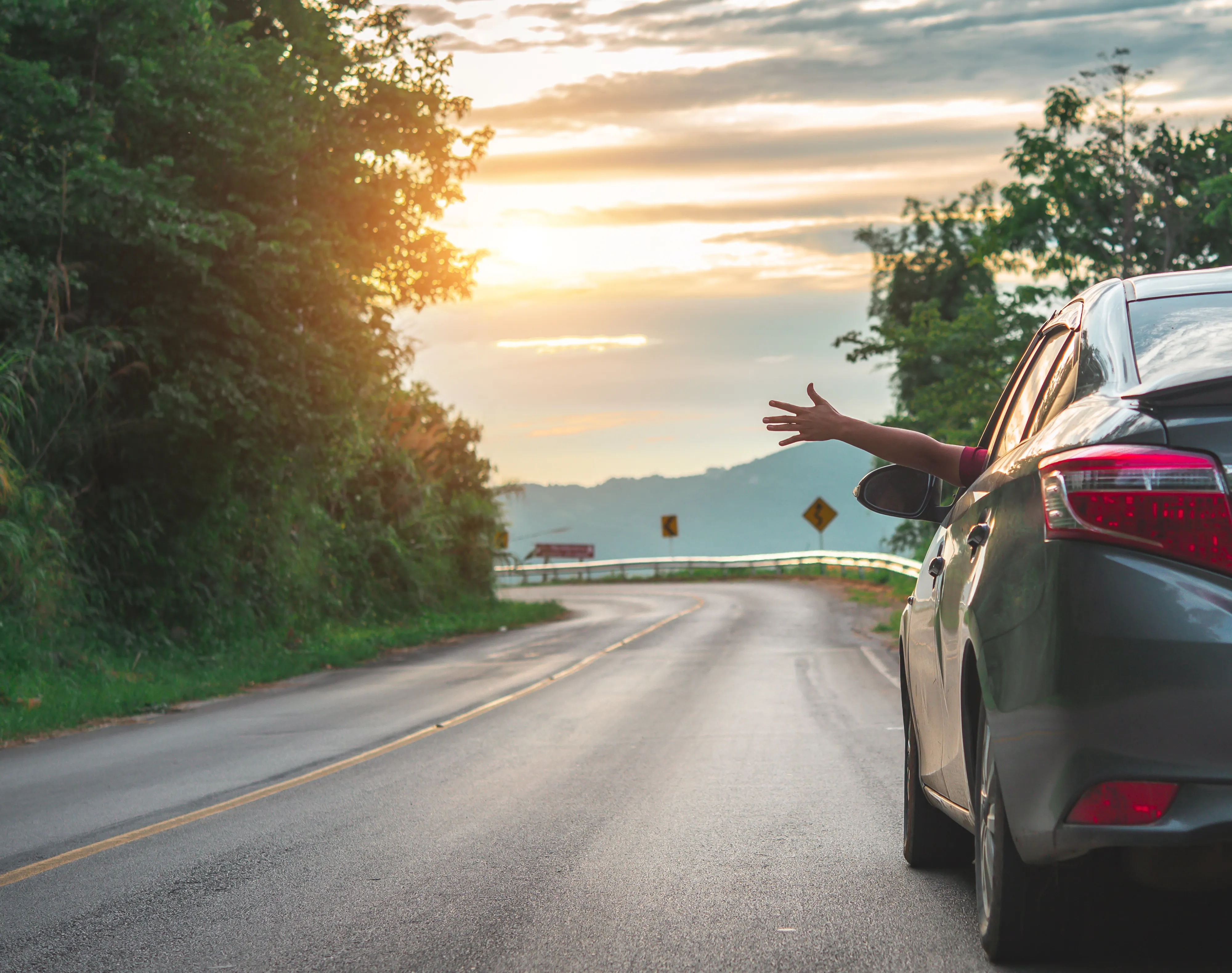 Car driving on the road with an arm sticking out of the window, summer sunset
