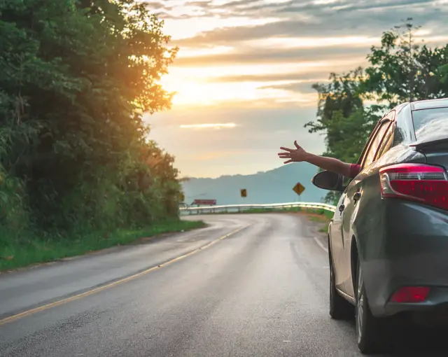 Car driving on the road with an arm sticking out of the window, summer sunset